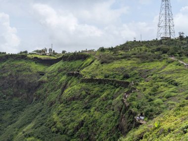 Rajgad Kalesi ve yemyeşil Sahyadri sırasının bulutlu muson yağmurlarının altında arka planda kulesi olan geniş bir manzarası.