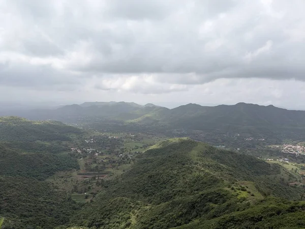 Geniş yeşil dağlar ve yoğun muson bulutları altında dağınık köy yerleşimleriyle bir vadi..