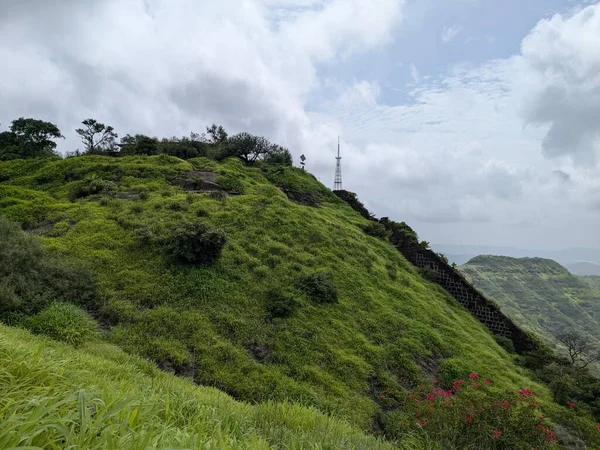 Gökyüzü bulutlu muson yağmurlarına karşı inşa edilmiş, uçuruma konmuş, haberleşme kuleleri olan yeşil bir tepe manzarası..