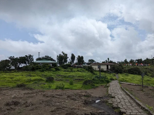 Sinhagad Kalesi 'nde bulutlu bir muson yağmuru altında yemyeşil tepelerle çevrili popüler bir bakış açısına giden manzaralı bir taş yol..
