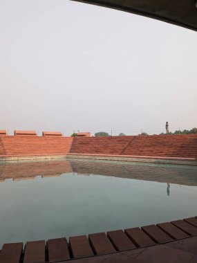 Delhi 'de ruhani ya da kültürel bir yerde, kırmızı taşlarla çevrili sakin bir havuzun geniş simetrik görüntüsü..