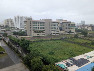 Geniş şehir manzarası, binaların yağmurdan sonra çimenli arazi ve ıslak yüzeyleri göstermektedir.