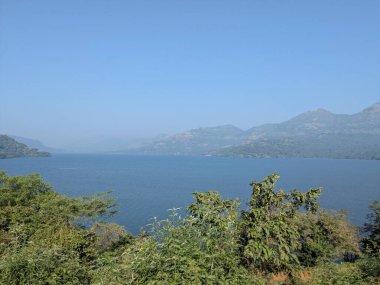 Yoğun yeşillik ve açık gün ışığında uzak tepelerle çevrili büyük tatlı su gölü.