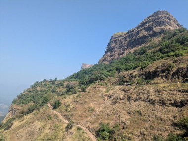 Geniş dağ vadisi manzarası ormanları tarlaları ve puslu mavi gökyüzünün altındaki yerleşimleri gösteriyor.
