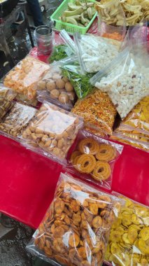 Çeşitli kızarmış atıştırmalıklar ve kurutulmuş yiyecekler bir sokak satıcı masasında şeffaf paketler halinde düzenlenir.