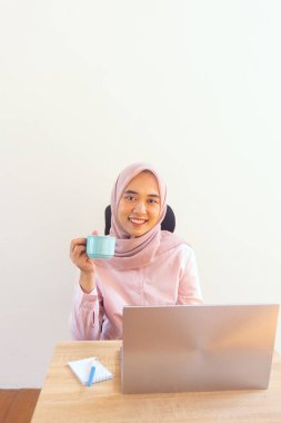 Genç jilbab kadın çalışırken kahvenin tadını çıkarıyor.