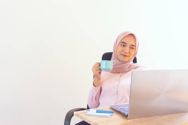 Genç jilbab kadın çalışırken kahvenin tadını çıkarıyor.