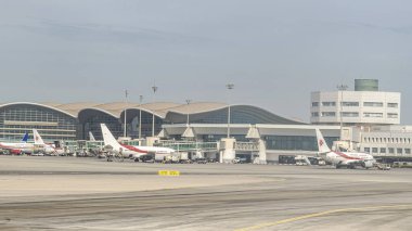 Cezayir, 1 Eylül 2025: Cezayir havayolları uçakları ve servis araçları Uluslararası Havaalanı Terminali önlüğü, bina cam cephe, bir kontrol kulesi ve jet köprüleri ile park.