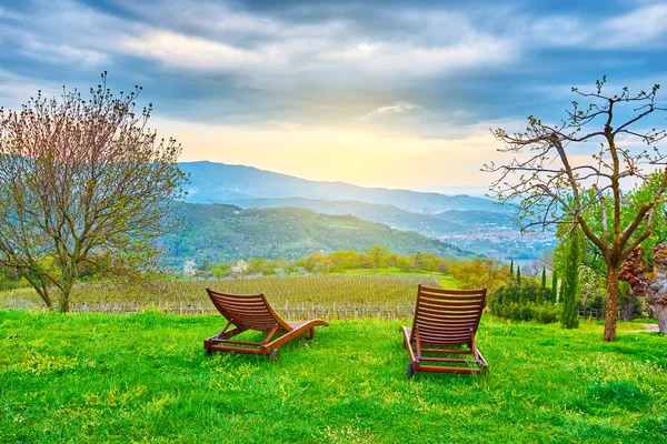 The two reclining chairs sit on the grass overlooking the valley and the hills after rain