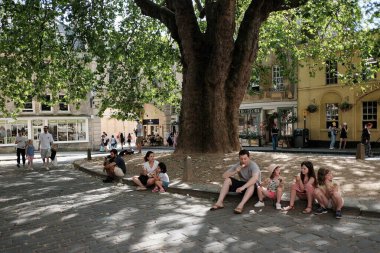 Bath, İngiltere - 29 Haziran 2019: İnsanlar şehir merkezindeki Abbey Green 'de bir çınar ağacının altında gölgeleniyor. Somerset 'teki ünlü Unesco Dünya Mirası kenti yılda 4 milyon ziyaretçi alıyor.