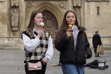 Bath, İngiltere - 12 Nisan 2021: İngiltere Covid-19 tecridini kısmen kaldırırken iki arkadaş Bath Abbey sahasında dondurmanın tadını çıkarıyor.