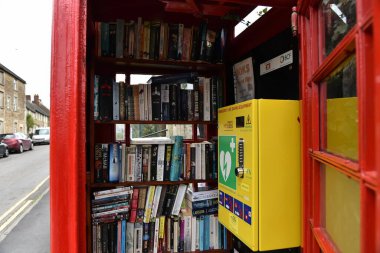 Rode, İngiltere - 4 Ekim 2017: Köydeki bir caddede kırmızı bir İngiliz telefon kulübesinde bir defibrilatör ve kitaplar görülüyor. İngiltere genelinde telefon kutuları kütüphanelere ve ilk yardım noktalarına dönüştürüldü.