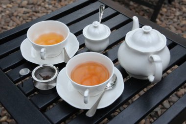 Bahçe kafesindeki ahşap bir masada porselen bir çaydanlıkla bir fincan çay.