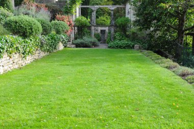 Mükemmel manikürlü yeşil bir çimen, taş sütunlar ve Akdeniz tarzı peyzaj tarafından çerçevelenmiş zarif bir taş bahçe terasına götürür. Bu sakin açık alan lüks gayrimenkul, lüks manzara tasarımı ve huzur dolu bir sığınak barındırıyor..