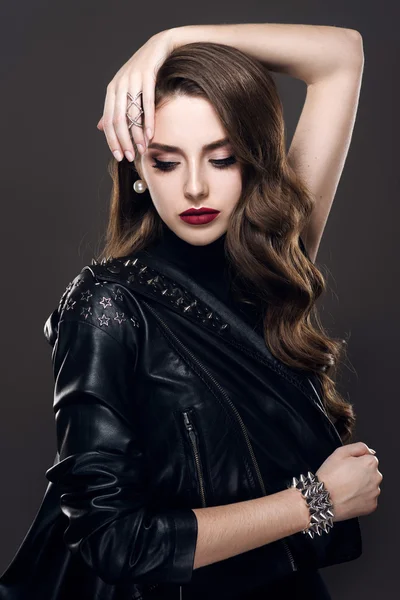 Гламурная молодая красивая рок-девушка в черной кожаной куртке с аксессуарами на темно-сером фоне — стоковое фото