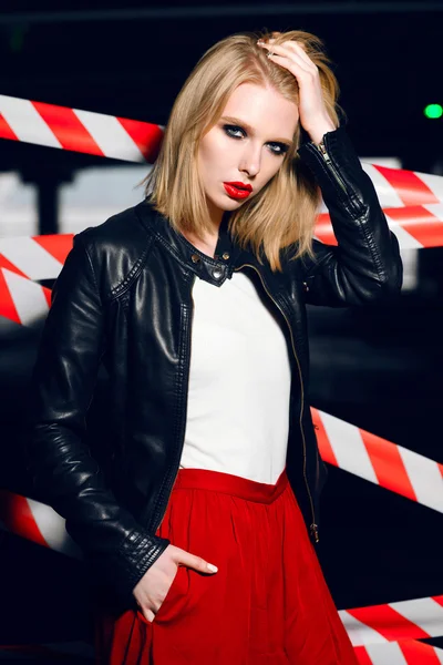 Mode portret van sexy blonde meisje met rode lippen dragen een rock zwarte stijl poseren op de achtergrond van de waarschuwing tape. — Stockfoto