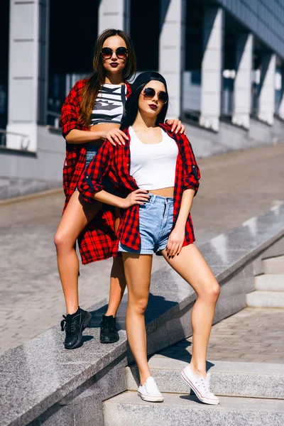 Dos chicas hipster felices jóvenes en gafas de sol que se divierten, sonriendo, riendo, saltando, caminando al aire libre en la calle, concepto de relax de verano —  Fotos de Stock