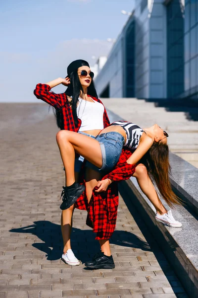 Dos chicas hipster felices jóvenes en gafas de sol que se divierten, sonriendo, riendo, saltando, caminando al aire libre en la calle, concepto de relax de verano —  Fotos de Stock