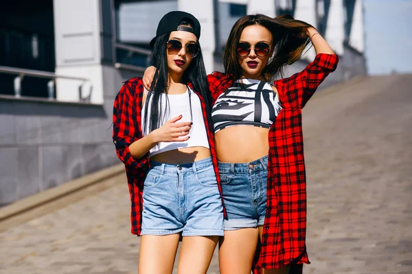 Две молодые счастливые девушки-хипстеры в солнцезащитных очках веселятся, улыбаются, смеются, прыгают, гуляют на улице, концепция летнего отдыха — стоковое фото