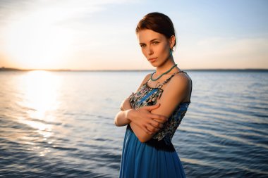 Gün batımında mavi gökyüzü karşı deniz sahilinde poz mavi elbiseli genç güzel kız