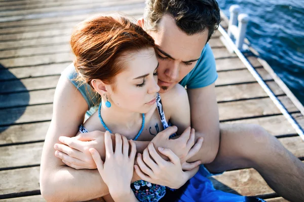 Feliz hermosa pareja caminando y abrazándose en la playa cerca del muelle al atardecer —  Fotos de Stock