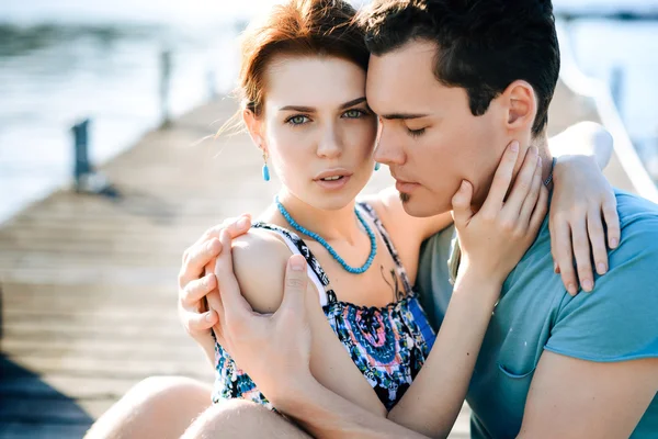 Feliz hermosa pareja caminando y abrazándose en la playa cerca del muelle al atardecer —  Fotos de Stock