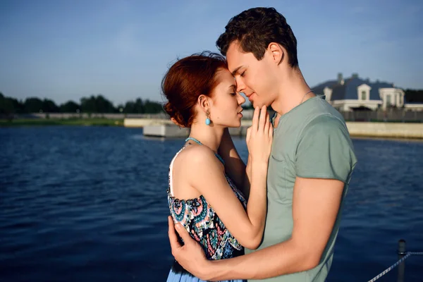 Feliz hermosa pareja caminando y abrazándose en la playa cerca del muelle al atardecer —  Fotos de Stock