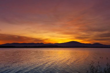 Sakin Göl 'ün Üzerinde Dağ Siluetiyle Canlı Gün Batımı