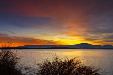 Sakin Göl 'ün Üzerinde Dağ Siluetiyle Canlı Gün Batımı