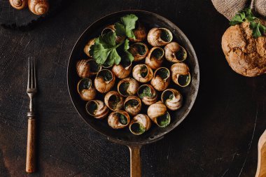 Ekmek ve doğal dokularla çevrili kırsal bir tavada otlarla süslenmiş salyangozun zarif sunumu yemek pişirme zevkini yaratıyor.