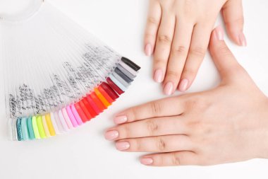 Renk paletinde çeşitli oje örnekleri sergileyen bir kadının elleri temiz beyaz arka planda, güzellik seçimlerini ön plana çıkarıyor.