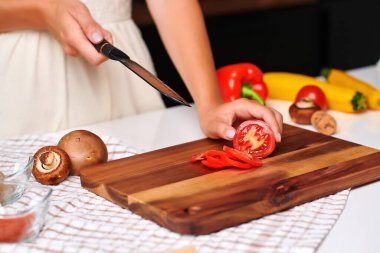 Kadın aşçı, renkli sebzeler ve temiz bir aşçılık ortamı ile çevrili, modern bir mutfakta ahşap bir kesme tahtasında ustalıkla taze domates ve dolma biber dilimliyor.