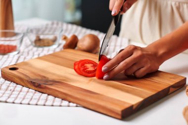 Kadın şef, parlak bir mutfakta ahşap bir kesme tahtasının üzerinde taze kırmızı bir domatesi ustalıkla dilimler. Mutfak tekniklerini ve canlı yemek hazırlama atmosferini vurgular.