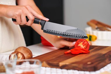 Kadın aşçı, modern bir mutfakta taze domates ve dolma biberleri ustalıkla dilimliyor. İçindeki canlı renkleri ve dokuları vurguluyor.