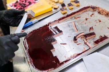 Pasta şefi paslanmaz çelik yüzeyinde çikolata ve böğürtlen içeren katmanlı tatlıyı kesiyor.