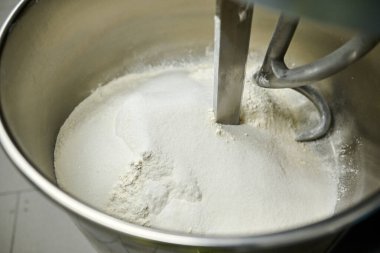 Karıştırma kabı beyaz un içerir ve karıştırma eklentileri, pişirme süreci ve çeşitli mutfak lezzetleri için hazırlanma örneklerini içerir