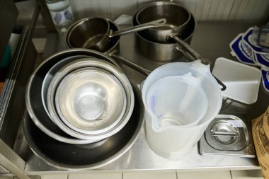 Mutfak tezgahında ölçüm kabının yanında paslanmaz çelik kaseler yığılmış, iyi organize edilmiş bir çalışma alanındaki temel mutfak araçlarını vurguluyor.