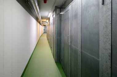 Metalik depolama birimleriyle kaplı koridor, yeşil bir zemin ve parlak ışıklandırma sergiliyor, uzayın modern endüstriyel atmosferini arttırıyor.