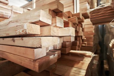 Bir depoda istiflenmiş ahşap tahtalar farklı boyutlarda ve dokularda sergileniyor, kerestenin doğal güzelliğini ve işçiliğini vurguluyor.