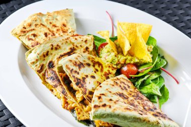 Taze salata ve gevrek tortilla cipsi eşliğinde gurme quesadilla, canlı renkler ve iştah açıcı bir düzende dokular vurgulanıyor.