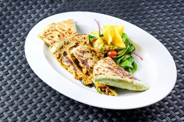 Taze salata ve simsiyah bir yüzeye konmuş tortilla cipsi ile servis edilen yumuşak ekmekler canlı renkleri ve çekici düzenlemeleri vurguluyor.