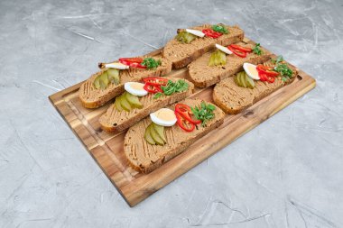 Bol soslu, turşu, kırmızı biber ve ahşap servis tahtasındaki yeşilliklerle süslenmiş ekmek dilimleri, mutfak keyfi için idealdir.