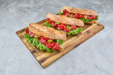 Marul, domates ve et gibi taze malzemelerle dolu üç iştah açıcı sandviç, ahşap bir tahtada güzelce sergilenmiş, mutfak sanatını ön plana çıkarıyor.