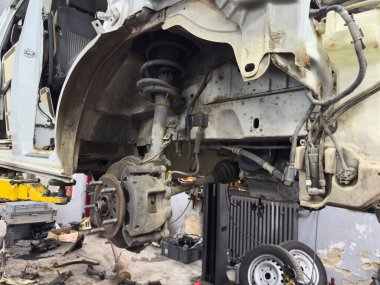 Otomotiv garajında parçalanmış araba süspansiyon sistemi mekanik parçaları ve araçları vurguluyor, dinamik ve çalışkan bir atmosfer yaratıyor.