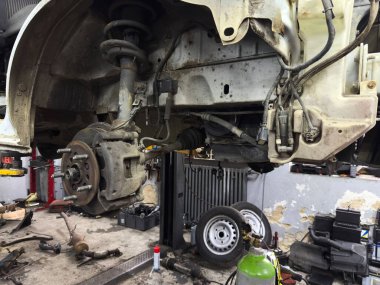 Otomobil süspansiyon sistemi garajda tamir ediliyor, mekanik parçaları ve araçları vurguluyor, dinamik bir otomotiv atölyesi atmosferi yaratıyor