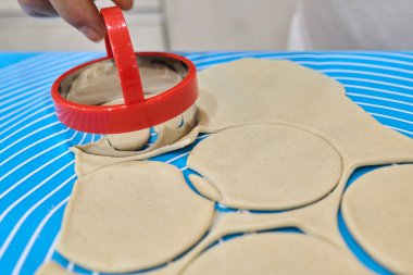 El, kırmızı dairesel kesiciyi mavi çizgili bir yüzey üzerinde hamura basıyor, bu da pişirme ve lezzetli yiyeceklere hazırlık sanatını gösteriyor.