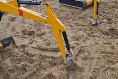 Kazı kolu kumlu zemini eşeliyor, inşaat sahasında görünür izler ve dokularla ağır makineler çalışıyor.