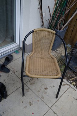 Çağdaş açık hava estetiğini vurgulayan bitki ve kiremitlerle çevrili, sağlam metal çerçeveli dokuma sandalye açık bir avluya yerleştirilir.