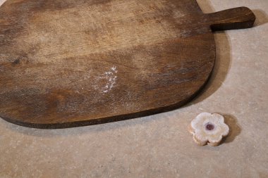 Kırsal ahşap kesim tahtasının dokusu, pürüzsüz bir taş yüzeyde çiçek şeklinde bir kurabiyenin yanında sergilenir. Mutfak vitrinleri için mükemmeldir.