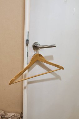 Ahşap askı kapı kolundan sarkıtılır, pratik kullanımı ve kapalı alan ortamında estetik çekiciliği vurgulanır.